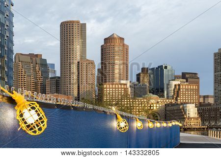 Lighted walkway near new construction along Harborwalk in South Boston with Rowes Wharf skyline in background
