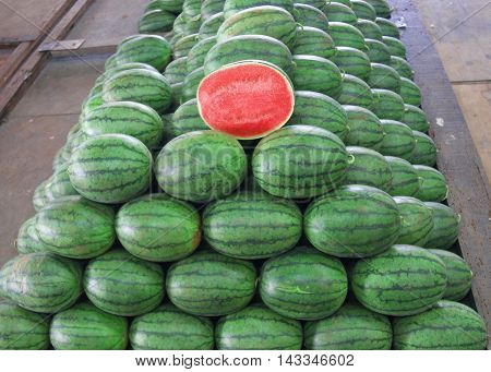 Many big sweet green watermelons and one cut watermelon.