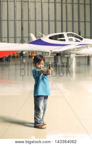 7 years old Asian boy dream to fly play flying toy in hangar with airplane background in vintage color