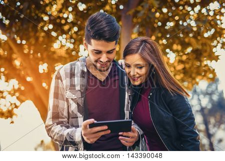 Young couple in the park during autumn season outdoor - using tablet technological device