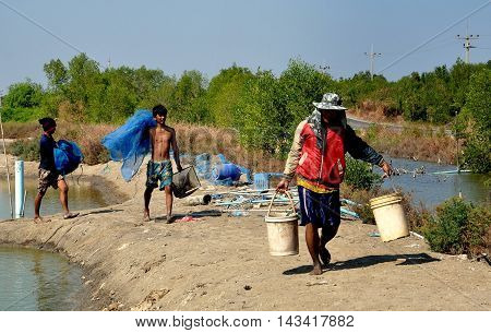Samut Songkhram Thailand - December 29 2011: Thai fishermen carrying buckets and nets heading for lunch after working the ponds at a local fish farm