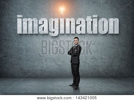 Businessman stands with his arms folded with big 3d 'imagination' word above. Ideas and concepts. Business staff. Office clothes. Intelligence and creativeness.