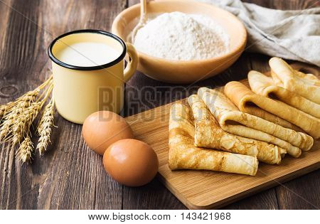 Fresh homemade crepes with ingredients and ears of wheat on rustic wooden background.