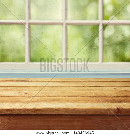 Empty wooden deck table and window with rain drops