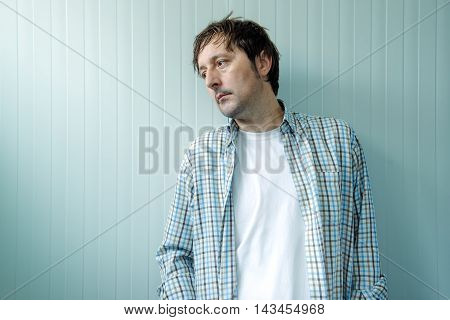 Sad and blue man male person with unhappy gloomy facial expression leaning on to wall and looking to a side.
