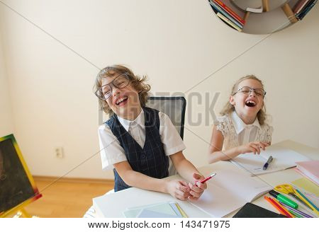 Disciples of an elementary school boy and girl are sitting at the same desk. Children are very fun they laugh. On the desk in children are school supplies and textbooks. Back to school.