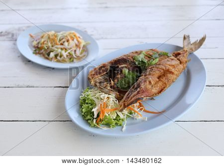 Fried Seriola fish in blue dish on wooden background.