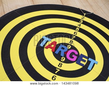 Close up word spell TARGET on dart board with wood background. (Selective focus)