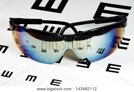 Sunglasses laying over an eyechart showing reflections of the letters