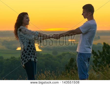 romantic couple holding hands at sunset on outdoor, beautiful landscape and bright yellow sky, love tenderness concept, young adult people