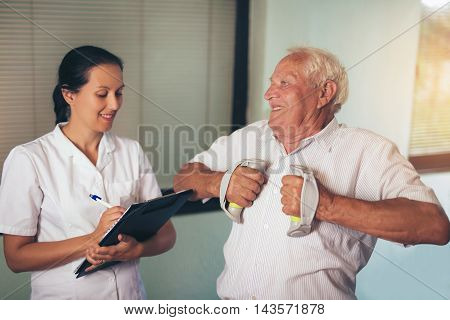 Senior man with dumbbells in rehab with a physiotherapist
