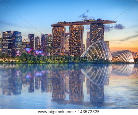 Singapore, Republic of Singapore - May 4, 2016: Supertree grove, Cloud garden greenhouse and Marina Bay Sands hotel reflecting in water at dusk with glowing lights