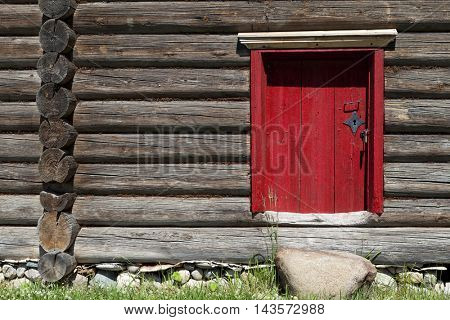 Beautiful old red door on the wooden wall of the old house. Lovely rustic background.