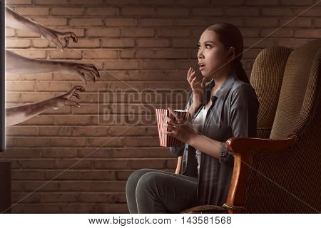 Asian Young Woman Watching Horror Movie And Eat The Popcorn With Sitting On Sofa