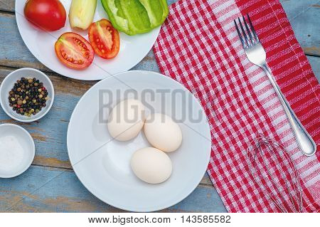 Fresh ingredients for omelet - three eggs in white plate vegetables and spices on the wooden rustic table