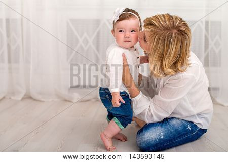 Young mother spending time at home with her little daughter. Mom and daughter dressed in white shirt and jeans