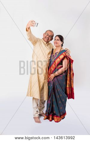technology and people concept - indian senior couple taking selfie with mobile camera, isolated over white background