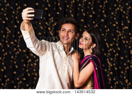 indian young Couple taking a self portrait or selfie using smart-phone in diwali festival