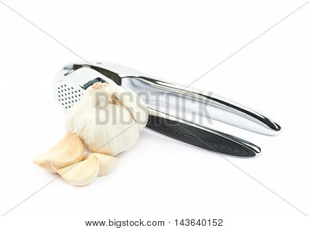 Metal garlic press utensil next to a pile of fresh cloves isolated over the white background