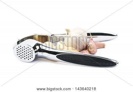 Metal garlic press utensil next to a pile of fresh cloves isolated over the white background