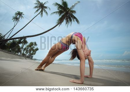 Young healthy fitness woman is doing yoga,standing in bridge pose(Setu Bandhasana) on the seaside