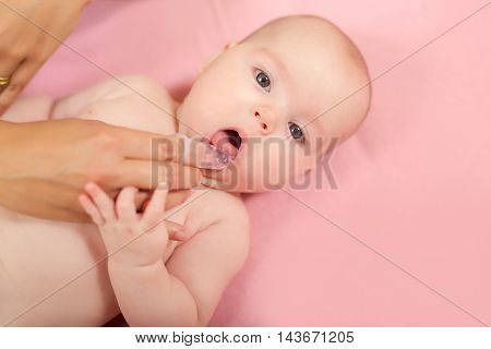 Mother cleaning baby`s mouth with special fingertip brush for children