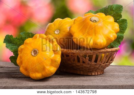 yellow pattypan squash with leaf in a wicker basket on a wooden table with a blurred background.