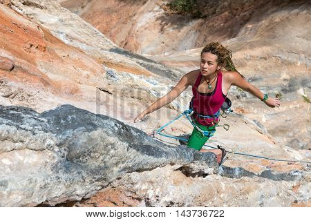 Portrait of Cute Girl rock Climber hanging on vertical orange wall energetic passionate Face Expression elegant Pose looking up orange and blue colour Stone Formations