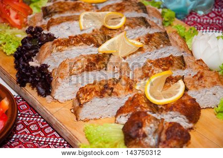 Meat pie on a wooden board decorated with lemon and herbs
