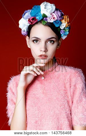 Beautiful model with a wreath of flowers on her head on red background