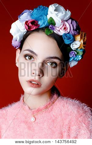 Beautiful model with a wreath of flowers on her head on red background