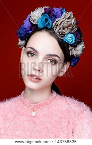 Beautiful model with a wreath of flowers on her head on red background