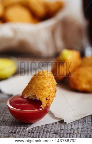 Homemade chicken nuggets on parchment paper with glass of cola and bowl with nuggets on background. Wood table. Nugget  in small glass of ketchup
