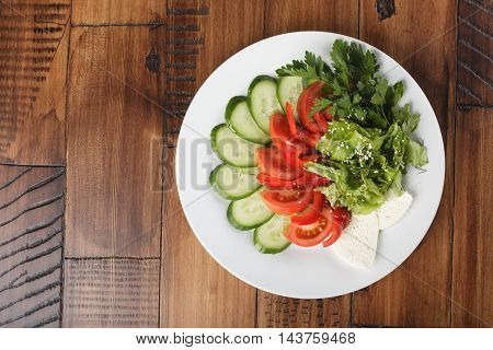 vegetable mix (salad, cucumber, tomato, parsley) and chees on a white plate. wooden background.