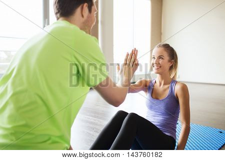 fitness, sport, training, teamwork and people concept - happy woman with personal trainer doing sit ups and high five gesture in gym