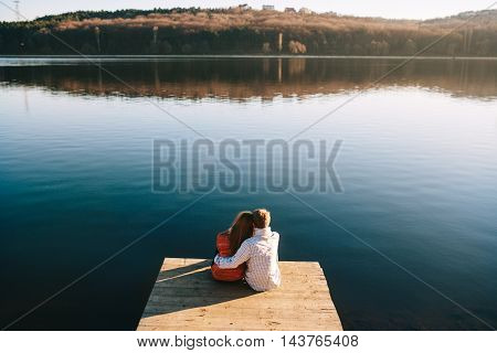 A young teens couple dreaming on the wooden jetty at a lake on a cold autumn day