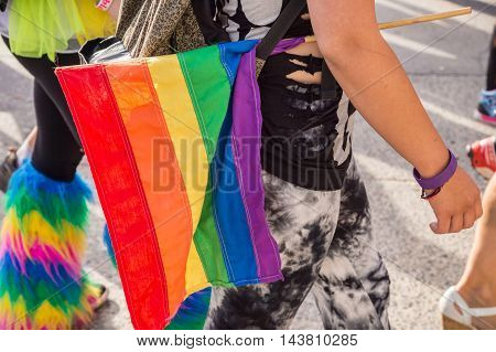 Side view of a walking girl hodling a gay rainbow gay flag under her arm at Montreal Pride Parade.