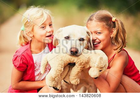 Sisters with dog. Two girls caress yellow labrador retriever with plush toy. - selective focus on the dog