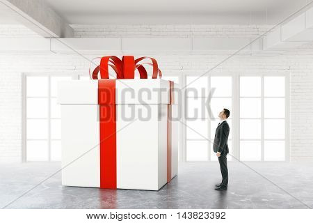 Businessman looking at huge present box in white brick interior. 3D Rendering