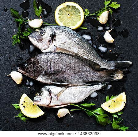 Fresh Fish Orata Over a Black stone with vegetables, lemon and pieces of ice. 
