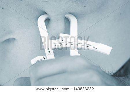Slim attractive young man using fat caliper to measure bodyfat on waist line.