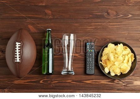TV remote control, beer and ball on wooden background