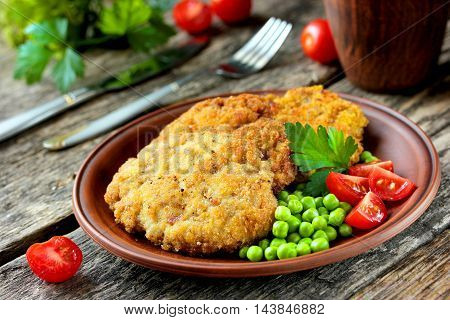 Delicious and hearty meal - fried steak in bread crumbs with tomatoes and green peas on a wooden table selective focus