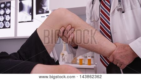 Senior caucasian doctor examining knee injury in his office