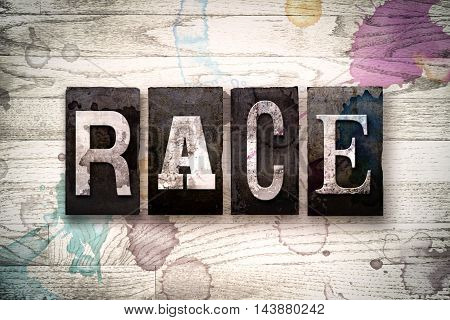 The word "RACE" written in vintage dirty metal letterpress type on a whitewashed wooden background with ink and paint stains.