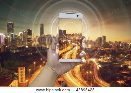 Hand holding white phone with city scape and wifi network connection concept .