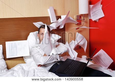 The hell with the job. Businesswoman throws documents. Man with laptop sitting on the couch with his arms crossed and fly papers around him. Deadline. Eff it!