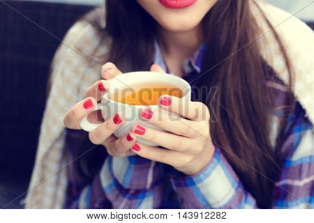 Girl wrapped in a blanket holding a cup of tea close-up in outdoor cafe