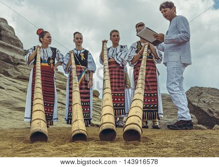 Bucegi Mountains Romania - August 6 2016: Romanian female tulnic players in traditional costumes pose near the Sphinx megalith on Bucegi mountains plateau. Shallow depth of field selective focus.