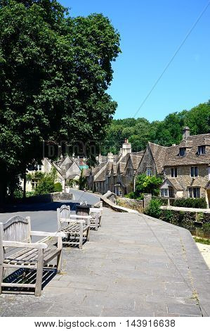 CASTLE COMBE, UNITED KINGDOM - JULY 20, 2016 - Stone cottages alongside the river Bybrook with wooden benches in the foreground Castle Combe Wiltshire England UK Western Europe, July 20, 2016.